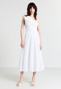 Abito bianco con corpetto aderente e gonna svasata, caratterizzato da ricami floreali. Design a spalla unica, abbinato a un paio di scarpe bianche open-toe.