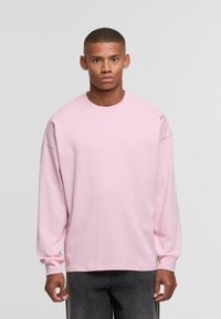 Lichtroze t-shirt met lange mouwen in een ontspannen pasvorm, met een ronde halslijn en ribgebreide manchetten, gemaakt van katoen. Heeft geen zichtbare logo's.