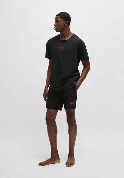 Ensemble t-shirt et shorts en coton noir avec un petit logo rectangulaire rouge sur la poitrine et sur les shorts, avec une coupe décontractée et un design simple.
