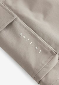 Tissu beige clair avec une texture lisse, présentant un bord replié et le mot "ACTIVE" en lettres blanches ; détails de design minimaux.