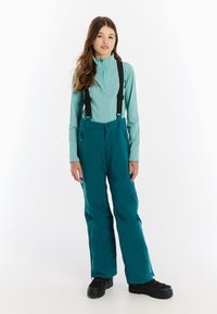 Tyrkysové lyžiarske nohavice s nastaviteľnými čiernymi traky, s vreckami na zips a zodpovedajúcim tyrkysovým dlhým rukávom s vysokým golierom.