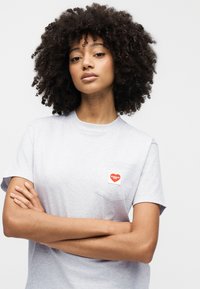 Γκρι βαμβακερό t-shirt με μικρό κόκκινο λογότυπο καρδιάς στην τσέπη του στήθους. Κοντά μανίκια και άνετη εφαρμογή με απαλό υφή.