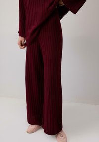 Burgundské pruhované kalhoty s širokými nohavicemi mají texturovaný pletený vzor. V kombinaci s světle růžovými teniskami nabízejí uvolněný střih a splývavou siluetu.