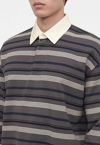 Jeune personne portant un maillot de rugby à manches longues rayé avec des bandes horizontales sombres et claires et un col clair contrastant.