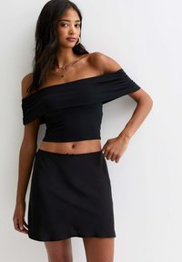 Zwarte off-the-shoulder crop top met gerimpelde mouwen, gecombineerd met een vloeiende zwarte mini-jurk met een strikdetail op de tailleband.