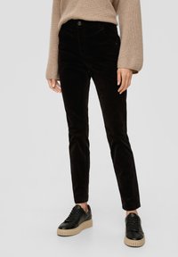 Pantalon en corduroy noir à coupe slim, avec poches avant et fermeture à bouton, associé à des baskets noires sur une plateforme beige.