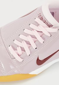 Pink patent leather sneaker with light pink laces, a maroon Nike logo, and a yellow sole. Features stitching and smooth texture.