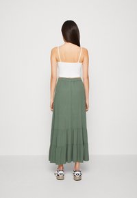 Jupe longue verte à volants en tissu léger, associée à un top blanc court et des baskets noires avec des accents beiges.