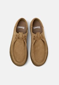 Zapatos casuales de ante marrón con punta redondeada, detalles cosidos y cierre con cordones. Interior suave y suela de goma.