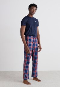 T-shirt à manches courtes marine avec un logo, associé à un pantalon de pyjama à carreaux rouges et bleus, avec une taille élastique et une coupe ample.