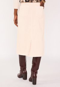 Jupe midi en velours côtelé beige clair avec une fente au dos, dotée de deux poches arrière et d'un tissu doux et texturé. Associée à des bottes hautes bordeaux.