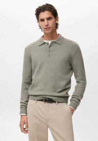 Maglione grigio chiaro lavorato a maglia con colletto, tre bottoni, polsini a coste e orlo, abbinato a pantaloni beige.