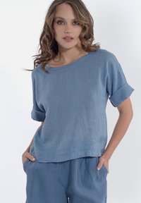 Top in lino leggero e blu con maniche corte arrotolate, scollatura ampia e vestibilità rilassata. Presenta una texture liscia e design informale.