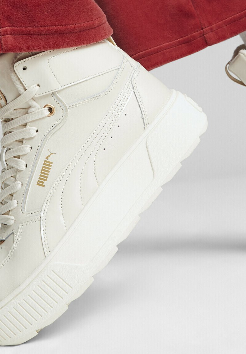 Białe sneakersy typu high-top z złotymi akcentami, z teksturowaną skórzaną cholewką, grubą białą podeszwą i widocznym logo na boku.