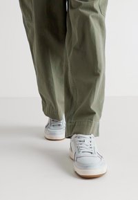 Pantalons larges verts en tissu léger, associés à des baskets bleu clair avec une semelle blanche et des détails de couture minimalistes.