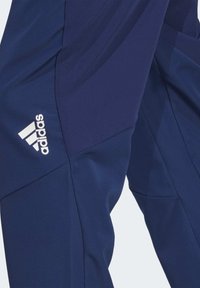 Marineblauwe sportbroeken van textuurstof, met contrasterende panelen en het witte Adidas-logo op de linker dij. Duurzaam en aansluitend ontwerp.