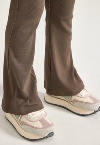 Ruske ribbede flared bukser parret med lyse sneakers med rosa og grønne accenter og en tekstureret sål.