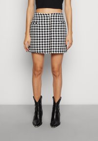 Mini-jupe à motif pied-de-poule noir et blanc avec fermeture boutonnée frontale et deux poches, associée à des bottines en cuir noir.