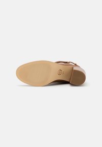 Zapato de tacón marrón con una parte superior de cuero suave, que presenta una suela de goma texturizada y una puntera redondeada, acentuada por pequeños detalles de metal.