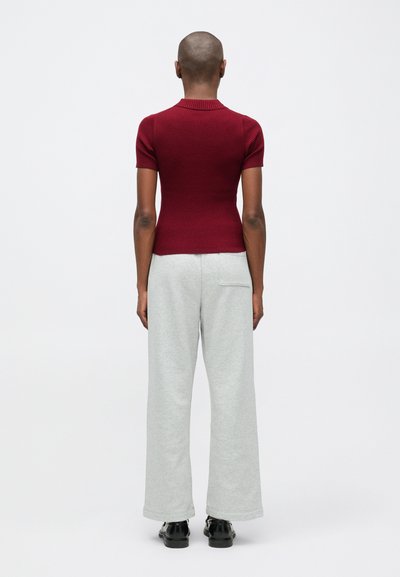 Ribēta bordo krāsas īsām piedurknēm blūze apvienota ar gaiši pelēkiem platām biksēm. Gluda tekstūra ar šuvju detaļu aizmugurējā kabatā. Melna apavi.