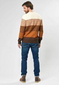 Knit sweater featuring horizontal stripes in cream, orange, brown, and dark brown, with a crew neck and ribbed hem. Worn over blue jeans.