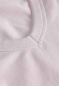 Gros plan sur un col en tissu coton rose clair avec bord-côte et couture double sur un vêtement.