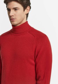 Röd polotröja i mjukt stickat material, med ribbat krage och sömlös axeldesign. Slät yta med minimal detaljering.