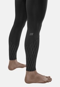 Zwarte aansluitende leggings met een diamantpatroon in grijs. Vergezeld door blote voeten, met een gladde textuur en elastische stof.