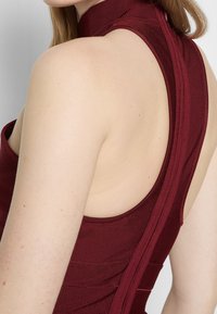 Burgundské bezrukávové tričko s vysokým límcem, které má texturovanou žebrovanou tkaninu a bezešvou konstrukci v oblasti zad a ramen.