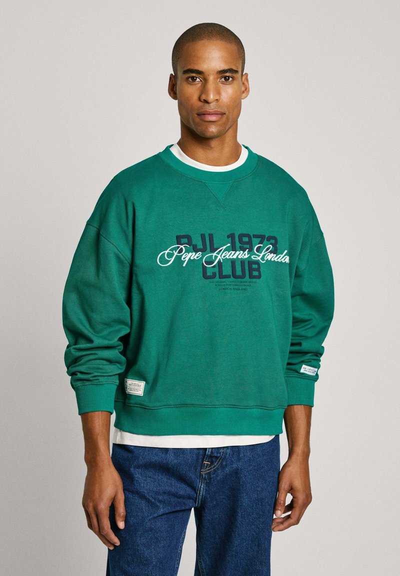 Sudadera verde con cuello redondo, que presenta el texto "PJL 1973 Pepe Jeans London CLUB" en azul marino y blanco. Tejido suave y corte relajado.