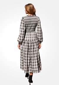 Langes Karokleid in Schwarz und Weiß, mit einem gerafften Rücken, voluminösen Ärmeln und einem fließenden Rock, getragen mit Ankle Boots.