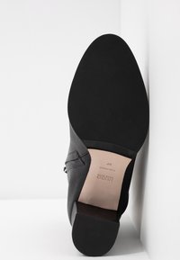 Semelle de chaussure en cuir noir avec l'avant noir texturé, zone de voûte beige lisse estampillée "Hugo Made in Italy 37" et talon bloc.