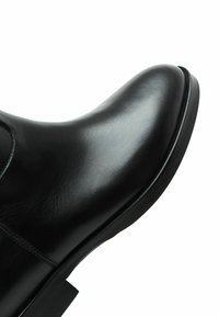 Scarpa in pelle nera con una superficie liscia, punta arrotondata, dettagli cuciti e una suola in gomma robusta. Si concentra su un design elegante e un aspetto senza soluzione di continuità.