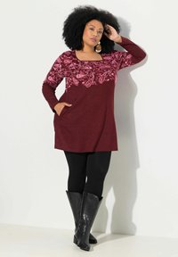 Burgundská tunika s paisley vzorem v růžové barvě na předním díle, dlouhé rukávy, boční kapsy, spárovaná s černými legínami a kozačkami po kolena.
