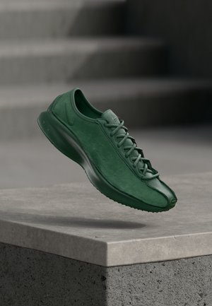 Grüner Sportschuh mit glatter Oberfläche, geschnürtem Design und abgerundetem Zehenbereich. Hergestellt aus mattem Material und mit einer flachen Silhouette ausgestattet.