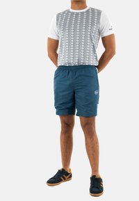 Conjunto masculino con una camisa de manga corta gris y blanca con estampado, pantalones cortos azules y zapatillas negras con acentos naranjas.