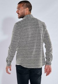 Herren Langarmhemd aus strukturiertem schwarz-weißem Strick, mit Stehkragen und knöpfbaren Manschetten, von hinten präsentiert.