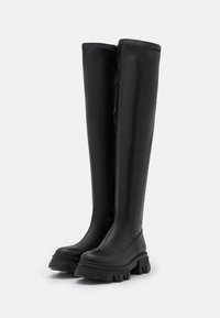 Knee-high black rubber boots with a matte finish, chunky rubber sole, and minimalistic design. Features a soft inner lining.