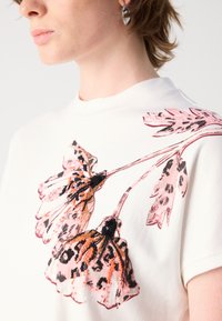 Witte t-shirt met korte mouwen, voorzien van een groot roze en zwart bloemenontwerp met geborduurde accenten op de voorkant en een hoge halslijn.