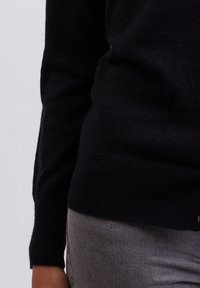 Suéter negro de cachemira con puños y dobladillo acanalados, combinado con jeans de mezclilla gris. Textura suave, diseño ajustado, costura del hombro visible.