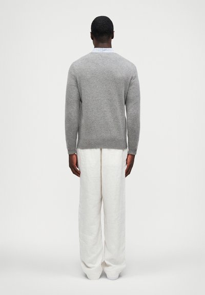 Suéter de lã cinza com gola redonda, barra canelada, combinado com calças largas de linho brancas. A vista traseira destaca a textura suave e o caimento.