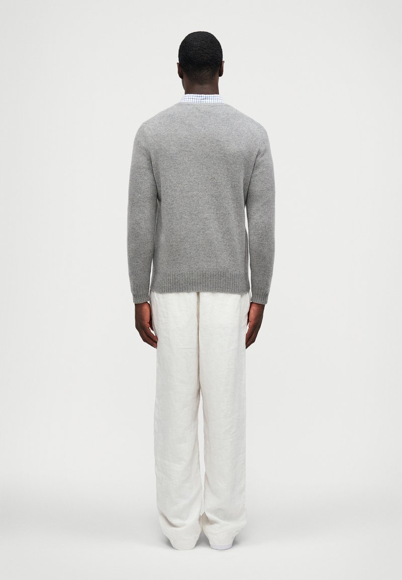 Jersey de lana gris con cuello redondo, dobladillo acanalado, combinado con pantalones anchos de lino blanco. La vista desde atrás resalta la suavidad de la textura y el ajuste.