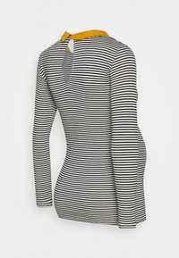 Långärmad topp i svart och vitt randigt mönster med en senapsgul krage, med en nyckelhålsutskärning på ryggen. Mjuk bomullsmaterial.