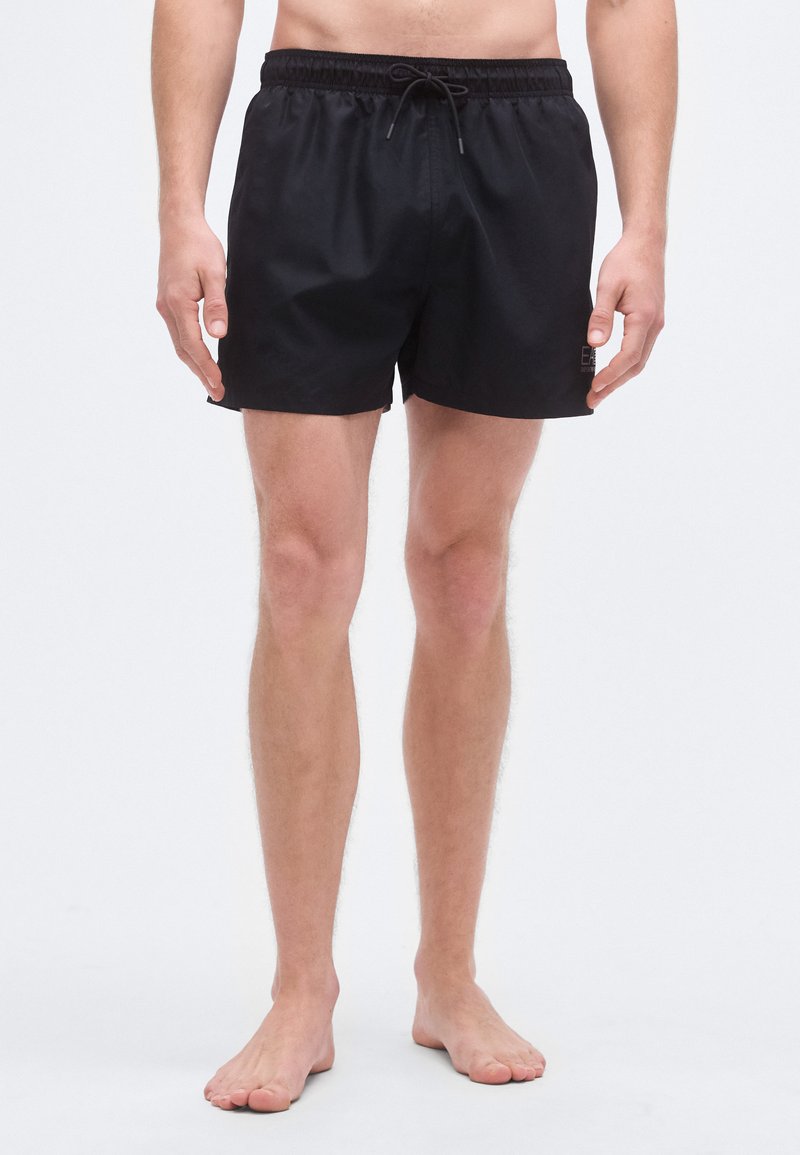 Juodi plaukimo šortai iš lengvos medžiagos, su elastinga juosmens juosta su raišteliu ir minimaliais prekės ženklo elementais šone.