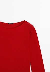 Pull rouge à manches longues avec un col rond, montrant le devant supérieur et une manche sur un fond blanc.