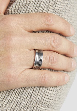 Close-up of a hand resting on beige knitted fabric, wearing a silver ring with a beaded middle band on the ring finger.