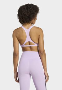 Reggiseno sportivo lilla con design a racerback e dettaglio ritagliato. Presenta linee eleganti e una texture liscia, abbinato a leggings coordinati.