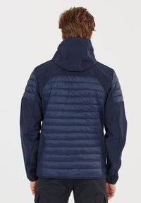 Marinblå jacka med en vadderad design på ryggen, fast huva och kontrasterande släta paneler på axlarna och ärmarna.
