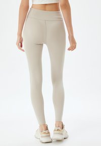 Beige high-waisted leggings, gemaakt van rekbare stof, aansluitend ontwerp, gladde textuur, gecombineerd met witte en beige sport schoenen.