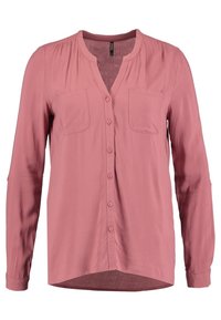 Blouse à manches longues rose poudré avec boutonnière sur le devant, deux poches poitrine, encolure ronde avec une petite découpe en V.